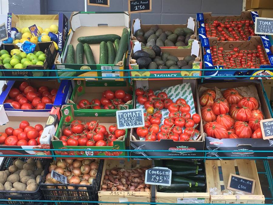 Étagères de légumes avec ardoises de prix manuscrites : courgettes, pommes de terre, oignons, échalotes, ail